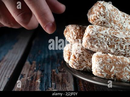 Bonbons, Datteln, die mit Kokosflocken bedeckt sind, auf einem schwarzen Teller über einem hölzernen Vintage-Tisch und einem dunklen Hintergrund Stockfoto