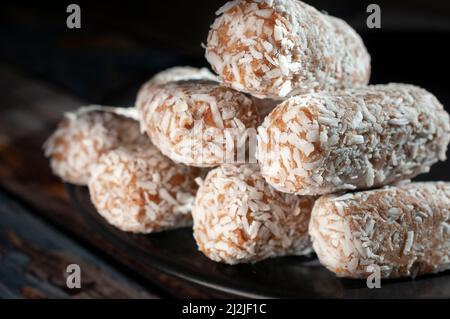 Bonbons, Datteln, die mit Kokosflocken bedeckt sind, auf einem schwarzen Teller über einem hölzernen Vintage-Tisch und einem dunklen Hintergrund Stockfoto