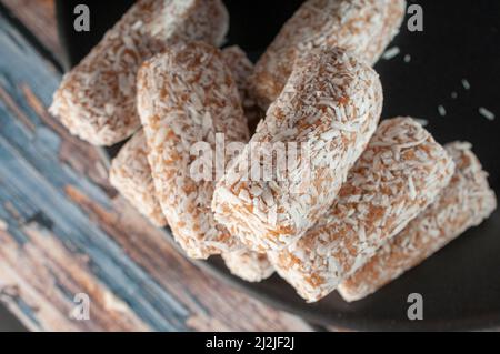 Bonbons, Datteln, die mit Kokosflocken bedeckt sind, auf einem schwarzen Teller über einem hölzernen Vintage-Tisch und einem dunklen Hintergrund Stockfoto