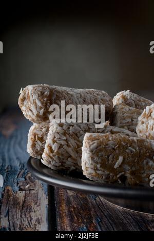 Bonbons, Datteln, die mit Kokosflocken bedeckt sind, auf einem schwarzen Teller über einem hölzernen Vintage-Tisch und einem dunklen Hintergrund Stockfoto