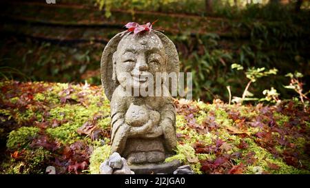 Nahaufnahme einer Steinstatue eines lächelnden Jizo Bosatsu, der eine Katze im Park hält Stockfoto