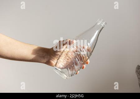 Nahaufnahme einer Glasflasche in der Hand eines Mannes gegen die graue Wand Stockfoto