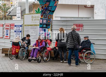 Netanya, Israel - 7. Februar 2022: Eine Gruppe älterer Menschen in Rollstühlen, die mit Sozialarbeitern im Park spazieren gehen. Nahaufnahme. Stockfoto