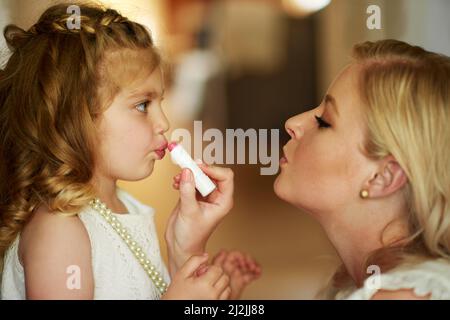 Verkleiden sich ihre kleine Prinzessin. Kurzer Schuss einer Mutter, die zu Hause Lippenstift auf ihre kleine Tochter anwendet. Stockfoto