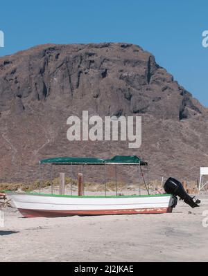 Ein Panga oder ein Boot auf dem Sand des Strandes mit einem großen Berg im Hintergrund mit einem blauen Himmel und einem sonnigen Sommermorgen in der schönen baja. Stockfoto