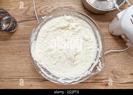 Fertig gemischter Hüttenkäse mit Schlagsahne für Käsekuchen in Glasschüssel, Draufsicht. Stockfoto