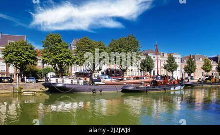 Dordrecht, Niederlande - Juli 9. 2021: Blick auf den typischen Binnenwasserkanal-Hafen mit altem Flachbodentransport und Raupenschiff gegen blaue Sommer s Stockfoto