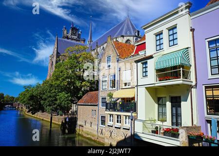 Blick auf den niederländischen Wasserkanal, am Wasser gelegene Wohnhäuser mit Balkonen und gotischem Kirchenhintergrund, blauer Sommerhimmel - Dordrecht, Niederlande Stockfoto