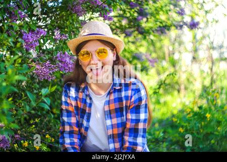 Lustiges Porträt. Unschärfe schöne junge Frau in der Nähe blühenden Frühlingsbaum. Fliederblüten im Busch. Jugend, Liebe, Mode, Romantik, Lifestyle-Konzept. Mädchen, ich Stockfoto