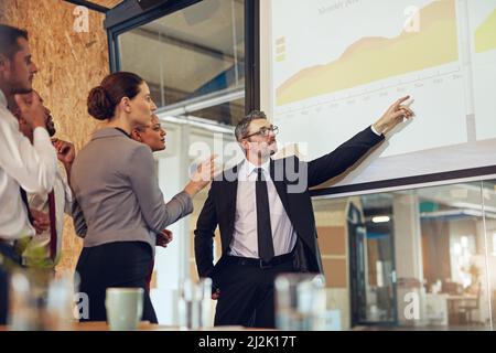 Mit seinem Team durch die Zahlen laufen. Aufnahme einer Führungskraft, die eine Präsentation auf einer Projektionsleinwand vor einer Gruppe von Kollegen in einem Sitzungssaal vorführt. Stockfoto