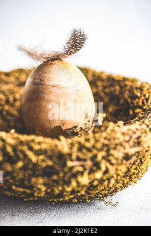 Feder auf einem goldenen Osterei in einem Vogelnest Stockfoto
