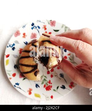 Die Hand der Frau hält einen halb gefressenen, mit Schokolade gefüllten Donut Stockfoto