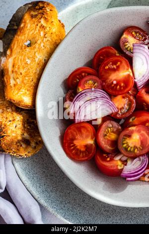 Nahaufnahme einer Schüssel mit Kirschtomaten und rotem Zwiebelsalat mit zwei Scheiben Toast Stockfoto