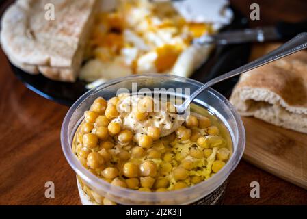 Hausgemachte Hummusschale, dekoriert mit gekochten Kichererbsen, Kräutern, Pita und Olivenöl auf einem rustikalen Metallhintergrund. Draufsicht.