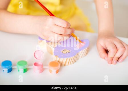 Nahaufnahme der Kinderhände mit einem Pinsel malt eine hölzerne Osterkaninchenfigur. Christliche Religion. Ukrainische Orthodoxie. Hochwertige Fotos Stockfoto