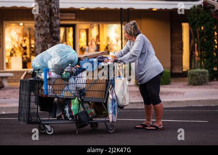 Alte obdachlose Frau, die mit ihren Habseligkeiten einen Einkaufswagen in der Innenstadt von Scottsdale, Arizona, USA, schiebt Stockfoto