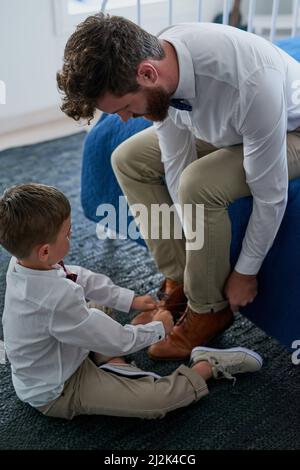 Helfen Sie dem Vatel, seine Schnürsenkel zu binden. Kurzer Schuss eines entzückenden kleinen Jungen, der zu Hause Schnürsenkel seines Vaters bindet. Stockfoto