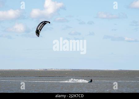 Norddeich, Deutschland. 02. April 2022. Bei sonnigem Wetter ist ein Kitesurfer an der Nordsee unterwegs, während die Insel Juist im Hintergrund zu sehen ist. Am 04.04.2022 beginnen die Osterferien in Niedersachsen, Bremen und Schleswig-Holstein. Quelle: Hauke-Christian Dittrich/dpa/Alamy Live News Stockfoto