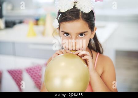 Es fühlt sich an, als würde ich die ganze Arbeit erledigen. Aufnahme eines entzückenden kleinen Mädchens, das bei ihrer Geburtstagsfeier einen Ballon in die Luft sprengen würde. Stockfoto