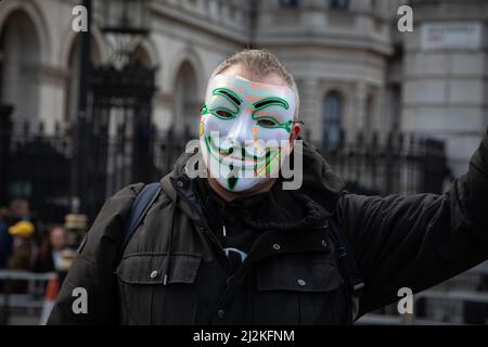 London, Großbritannien. 2. April 2022. Ein Mann mit einer anonymen Maske schwenkt eine Flagge vor der Downing Street, wo sich Menschen versammelt haben, um gegen die steigenden Lebenshaltungskosten im Land zu protestieren. Quelle: Kiki Streitberger/Alamy Live News Stockfoto