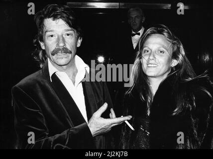 Der britische Schauspieler John Hurt kommt mit seiner Frau Donna in der Royal Albert Hall in London an, um das Musical "The Hunting of the Snark" zu besuchen, das auf Lewis Carrolls Gedicht basiert und vom Komponisten Mike Batt geschrieben wurde, wobei John Hurt die Narration zur Verfügung stellte. 1.. April 1987. Stockfoto