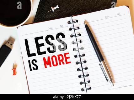 Mehr oder weniger in Notizbuch auf Holzschreibtisch mit Markierstift und Brille geschrieben. Draufsicht Stockfoto