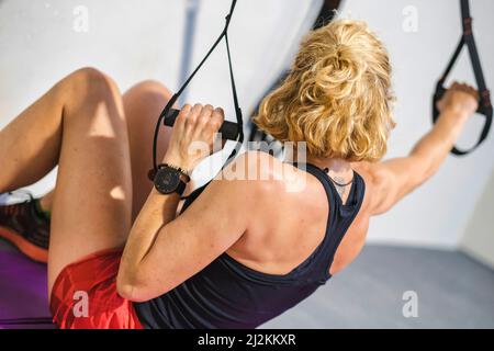 Echte junge reife kaukasische Frau in einer Sportkleidung im Fitnessstudio Training Arme Übungen mit trx Fitness-Riemen. Fitnesskonzept. Stockfoto