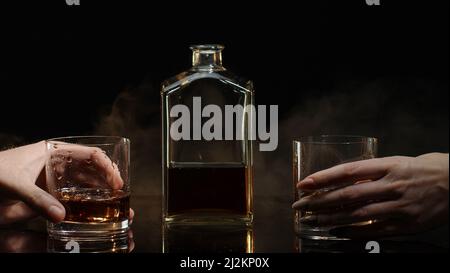 Zwei Hände mit Gläsern Cognac-Whiskey mit Eiswürfeln, die auf schwarzem Hintergrund Prost-Toast machen Stockfoto