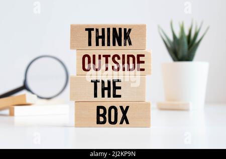 Denken Sie außerhalb des auf Holzblock geschriebenen Kastenworts. Denken Sie außerhalb des Kastentextes auf Holztisch an Ihr Desing, Top View Konzept. Stockfoto