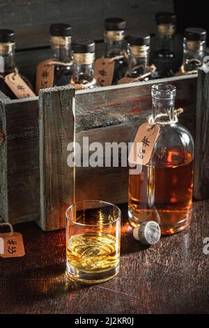 Guter und gealterter Cognac und Holzkiste mit Flaschen in der Destillerie. Glas Whisky mit Eis in einem alten Keller. Stockfoto