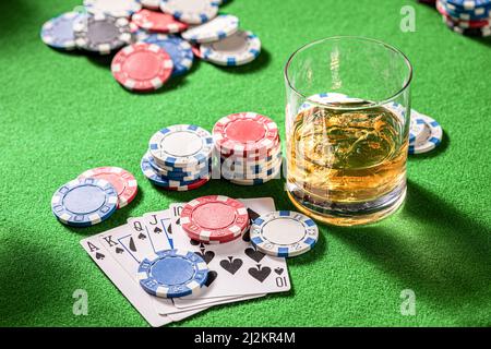 Grüner Spieltisch mit Whisky, Karten und Chips. Glas Bourbon mit Eis auf Spieltisch mit Karten und Chips. Stockfoto
