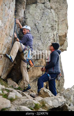 Männer im Sicherheitsgeschirr klettern Klippe in den Bergen Stockfoto