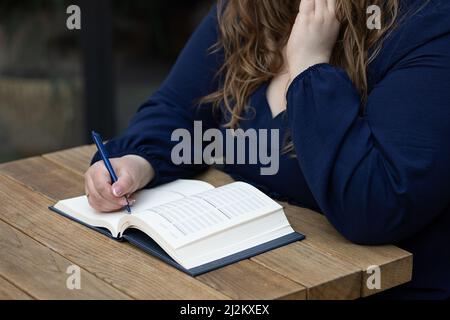 Nahaufnahme beschäftigt Frau Schreiben und Notizen in Notizbuch halten Stift. Handschrift auf dem Schreibtisch am Arbeitsplatz, dunkler unscharfer Hintergrund, selektiver Fokus, frei Stockfoto