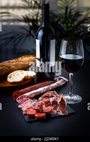 Spanischer Snack mit Chorizo, Salchichon, Jamon, frischem Baguette und einem Glas Rotwein. Stockfoto