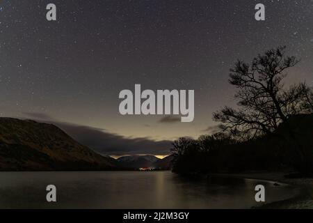 Ein Blick auf den Nachthimmel über Ullswater im englischen Seenland mit Schnee, der die fernen Berge bedeckt Stockfoto