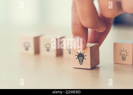 Idee und Kreativität Konzept. Männliche Hand hält Holzwürfel mit Glühbirnen Symbol auf hellem Hintergrund. Teamwork Brainstorming Ideen, Bewertung und Selec Stockfoto