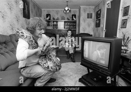 Als sich der Schlangenliebhaber Tony Griffiths mit Monty, seinem Haustierpython, einlässt, um fernzusehen, bewegt sich seine Frau Marilyn so weit wie möglich weg. Sie leben in Ladywood. 13.. Februar 1990. Stockfoto