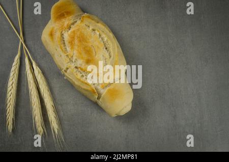 Schönes Sauerteigbrot auf grauem Hintergrund mit getrockneter Weizenblume. Stockfoto