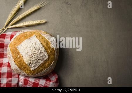 Schönes Sauerteigbrot auf grauem Hintergrund mit getrockneter Weizenblume. Stockfoto