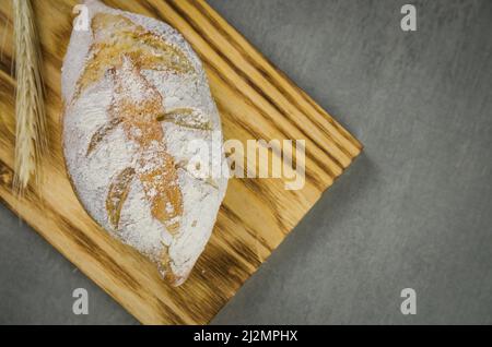 Schönes Sauerteigbrot auf grauem Hintergrund mit getrockneter Weizenblume. Stockfoto