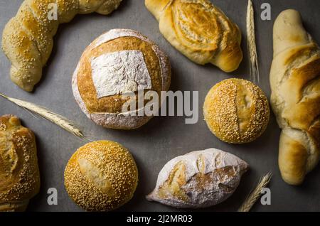 Schönes Sauerteigbrot auf grauem Hintergrund mit getrockneter Weizenblume. Stockfoto