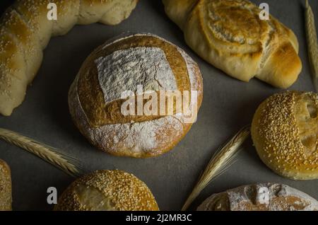 Schönes Sauerteigbrot auf grauem Hintergrund mit getrockneter Weizenblume. Stockfoto