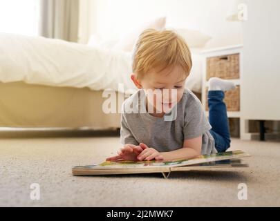 Im langsam lernen, alle großen Worte jetzt zu lesen. Aufnahme eines Jungen, der zu Hause ein Buch liest. Stockfoto