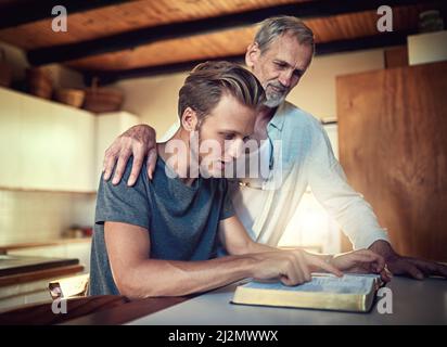 Sie ist eine Familie, die im Glauben gestärkt wurde. Aufnahme eines Vaters und eines Sohnes, die zu Hause gemeinsam Bibelstudien machen. Stockfoto