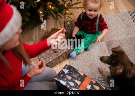 Ein zweijähriges Kind sitzt auf dem Boden und füttert einen Mischlingshund mit Leckereien. Stockfoto