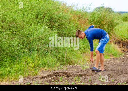 Junger Mann gräbt mit Schaufel im Garten Boden, lockert Boden zum Pflanzen von Gemüse. Home Gemüsegarten auf dem Land Stockfoto