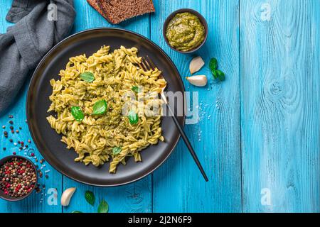 Pasta mit Pesto-Sauce und frischen Basilikumblättern auf blauem Hintergrund. Stockfoto