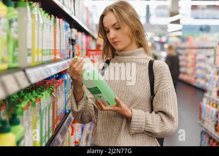 Junge Frau wählt Waschmittel-Gel oder Conditioner für die Waschmaschine im Haushalt zu speichern. Stockfoto