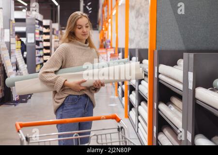 Junge Frau wählen Tapete im Baumarkt. Home Design und Renovierungskonzept Stockfoto