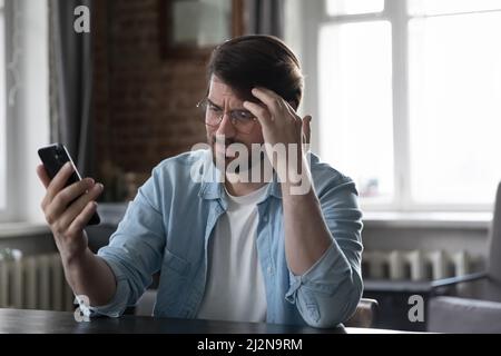 Besorgt verärgerten Mann starrte auf Handy-Bildschirm mit verärgerten Gesicht Stockfoto